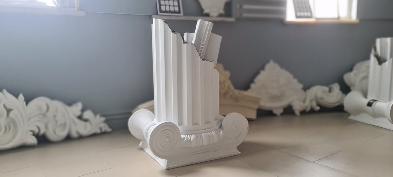 Poliuretan Coloane Ionice si Elemente de Montaj Coloana din poliuretan reprezintă un element decorativ arhitectural de înaltă densitate, utilizat pentru îmbrăcarea stâlpilor de susținere sau pentru crearea de fațade clasice la exterior. Modelul prevăzut cu caneluri verticale și bază de stil ionic P5240I asigură o integrare vizuală precisă în proiectele rezidențiale și comerciale. Structura modulară permite combinarea profilului de corp P5840 cu bazele din seria P5940B, simplificând semnificativ procesul de montaj în șantier.

Din punct de vedere al punerii în operă, grosimea peretelui profilului este de aproximativ 15-20 mm, lăsând un miez gol în interior pentru a permite mascarea facilă a structurilor din beton armat sau țevi metalice. Fixarea se realizează prin lipire structurală cu adeziv poliuretanic special și ancorare mecanică suplimentară. Lipiturile între secțiuni se îmbină perfect, fiind șlefuite cu hârtie abrazivă de granulație 180-240 înainte de aplicarea amorsei și a vopselei lavabile de exterior.

Spre deosebire de ipsos sau beton decorativ, materialul are o densitate optimă de 150-220 kg/m³ (țintă ~160 kg/m³) și un coeficient de absorbție a apei de sub 0.1%, eliminând riscul de fisurare la îngheț. Produsul rezistă eficient la variații termice extreme cuprinse între -100 °C / +80 °C, menținându-și stabilitatea dimensională în timp. Greutatea redusă a pieselor poliuretanice elimină încărcarea suplimentară pe structura de rezistență a clădirii, reducând totodată timpul de manoperă cu până la 50%.

Acest sistem modular de coloane poliuretanice este pregătit din fabrică cu un strat de amorsă albă, optimizat pentru aderența vopselei acrilice sau poliuretanice. Este soluția tehnică ideală pentru firmele de construcții și montatori care caută o alternativă durabilă, rezistentă la razele UV și ușor de prelucrat cu unelte standard de tâmplărie.