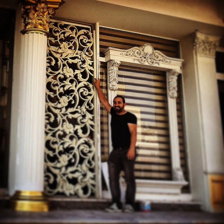 Panouri Decorative și Elemente din Poliuretan Exterior Panoul decorativ din poliuretan rigid de înaltă densitate este un element arhitectural utilizat pentru finisarea fațadelor exterioare și structurilor de placare decorative. În această aplicație tehnică, panoul perforat P8110 este fixat pe structura de suport verticală, asigurând o rezistență ridicată la variațiile de temperatură cuprinse între -100 °C / +80 °C. Densitatea materialului de aproximativ 150-220 kg/m³ (țintă ~160 kg/m³) oferă stabilitate dimensională excelentă, fără riscul de deformare cauzat de umiditate sau radiațiile UV. Utilizarea profilurilor din poliuretan la exterior elimină punțile termice și reduce sarcina structurală pe fațadă în comparație cu elementele tradiționale din ipsos sau beton.

Procesul de montaj al ancadramentelor și al coroanei P2839 necesită o pregătire riguroasă a suprafeței suport prin curățare și amorsare. Pentru fixare mecanică și chimică, se recomandă aplicarea unui adeziv poliuretanic structural monocomponent în tub de 310 ml, combinat cu dibluri de ancorare mascate în corpul profilului. Consola P9925 funcționează ca element de susținere vizuală sub profilul de coronament, necesitând o îmbinare etanșă cu spumă adezivă specială pentru exterior. Rosturile dintre piese se etanșează cu un chit poliuretanic flexibil pentru a preveni infiltrațiile de apă și fisurarea în zonele de îmbinare supuse dilatării termice.

Finisajul de protecție al elementelor decorative din poliuretan constă în aplicarea unui strat primar de amorsă acrilică, urmat de două straturi de vopsea lavabilă de exterior rezistentă la intemperii. Suprafața densă a poliuretanului nu absoarbe apa, având o rată de absorbție a umidității sub 1%, ceea ce împiedică apariția igrasiei și deteriorarea cauzată de ciclurile de îngheț-dezgheț. Coloana ornamentală integrată în ansamblu beneficiază de finisaj acrilic și accente decorative realizate cu vopsea acrilică metalizată, protejată cu lac poliuretanic transparent pentru o durabilitate crescută în timp.

Alegerea profilurilor din poliuretan în proiectele de renovare sau construcție nouă oferă avantaje majore pentru echipele de montaj și constructori. Datorită greutății reduse, manevrarea și debitarea elementelor precum P8110 sau P2839 se realizează rapid pe șantier folosind scule obișnuite de tâmplărie. Sistemul modular permite ajustarea precisă pe dimensiunile ferestrelor și ale intrărilor, asigurând un timp de execuție redus cu până la 50% față de soluțiile clasice din piatră sau stucatură cimentată, menținând în același timp standarde ridicate de durabilitate.