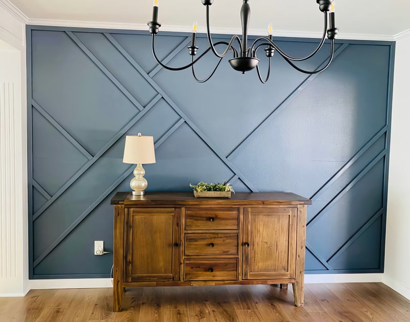Montaj Baghete Poliuretan pentru Perete Geometric Modern Animația de perete accent realizată din profile din poliuretan reprezintă o soluție tehnică durabilă și stabilă pentru crearea structurilor decorative liniare pe suprafețe verticale în amenajările interioare. În acest proiect, s-a utilizat profilul din poliuretan P851350, având o lățime standard de 40 mm și o grosime de 15 mm, montat direct pe placa de gips-carton. Materialul se remarcă printr-o densitate ridicată de aproximativ 150-220 kg/m³ (țintă ~160 kg/m³), oferind rezistență sporită la impact mecanic și stabilitate dimensională excelentă în medii cu variații de temperatură între -100 °C / +80 °C. Spre deosebire de profilele din lemn sau MDF, poliuretanul prezintă un coeficient de absorbție a apei de sub 1%, ceea ce împiedică umflarea sau deformarea îmbinărilor în timp.

Procesul de debitare și îmbinare la unghi necesită instrumente profesionale de tăiere pentru a asigura îmbinări invizibile la unghiuri de 45 de grade și 90 de grade în punctele de intersecție diagonală. Baghete din poliuretan P851350 sunt fixate mecanic și chimic pe perete folosind un adeziv de montaj pe bază de polimeri hibrizi cu aderență inițială mare. Pentru realizarea rosturilor perfecte, îmbinările dintre profile se tratează cu adeziv special pentru îmbinări, urmat de o șlefuire fină cu hârtie abrazivă cu granulație de 240 după uscarea completă. Geometria asimetrică creată necesită o trasare prealabilă pe perete cu nivela laser, garantând alinierea perfectă a liniilor intersectate pe întreaga suprafață a peretelui.

Aplicația finală implică pregătirea suprafeței prin aplicarea unui grund acrilic peste profilele din poliuretan P851350 și suprafața peretelui, urmată de vopsirea în două straturi cu vopsea lavabilă mată într-o nuanță intensă de albastru petrol. Profilele din poliuretan vin pre-grunduite din fabrică, reducând consumul de vopsea și facilitând o aderență uniformă a stratului de finisaj fără risc de exfoliere. Vopsirea integrală a peretelui și a profilului în aceeași culoare creează un efect arhitectural monolit, unde jocul de lumini și umbre oferă adâncime vizuală fără a încărca spațiul. Finisajul uniform protejează structura împotriva acumulării de praf și permite o curățare facilă cu o lavetă umedă.

Pentru meșterii montatori și firmele de reamenajare, utilizarea poliuretanului de înaltă densitate oferă avantaje majore în comparație cu ipsosul clasic sau profilele din MDF. Greutatea redusă a fiecărui profil din poliuretan permite un montaj rapid de către o singură persoană, reducând timpul de manoperă cu până la 30%. În plus, elasticitatea moderată a poliuretanului permite preluarea micilor denivelări ale peretelui suport fără a se fisura. Structura sintetică omogenă asigură o debitare curată fără așchiere, ceea ce eficientizează procesul de șlefuire și scurtează durata totală de execuție a proiectului de amenajare.