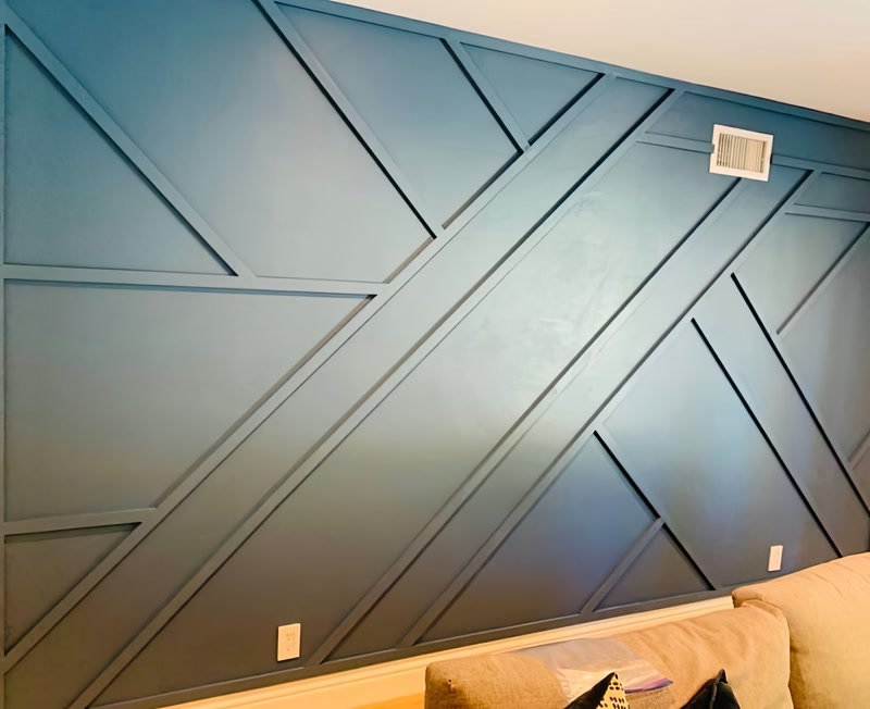 Profil Poliuretan P851350 cu Design Geometric pe Perete Peretele accent decorat cu profile din poliuretan P851350 reprezintă o soluție tehnică modernă și rezistentă pentru structurarea spațiilor interioare prin modele geometrice complexe. Spre deosebire de lambriurile sau riflajele din lemn tradițional sau MDF, profilele poliuretanice de înaltă densitate (aproximativ 150-220 kg/m³ (țintă ~160 kg/m³)) oferă o stabilitate dimensională absolută, fără risc de deformare sau fisurare în timp din cauza variațiilor de umiditate. Structura fină a materialului permite obținerea unor muchii extrem de precise și tăieturi curate în unghiuri ascuțite, esențiale pentru îmbinările diagonale specifice acestui tip de aplicație.

Procesul de instalare a profilelor decorative din poliuretan P851350 necesită o trasare geometrică riguroasă pe suprafața peretelui înainte de debitare. Se recomandă utilizarea unui ferăstrău cu pânză fină sau a unui circular cu reglaj de unghi pentru a realiza tăieturi exacte la 30, 45 sau 60 de grade. Fixarea elementelor pe suportul mecanic se execută direct cu adeziv structural pe bază de polimeri hibrizi, care asigură o priză rapidă și o aderență excelentă. În zonele de îmbinare dintre baghete, aplicarea unui adeziv special pentru rosturi împiedică apariția microfisurilor ulterioare.

Etapa de finisare tehnică este crucială pentru obținerea unui aspect monolitic pe peretele accent. După uscarea completă a adezivului (aproximativ 24 de ore), îmbinările se șlefuiesc ușor cu hârtie abrazivă de granulație 240 pentru a elimina orice denivelare. Suprafața profilelor poliuretanice P851350 este deja amorsată din fabrică, permițând aplicarea directă a vopselei lavabile pe bază de apă, acrilice sau latex. Absorbția de apă a poliuretanului de sub 1% garantează o aplicare uniformă a straturilor de vopsea, fără a afecta structura internă a baghetelor.

Alegerea profilului din poliuretan P851350 optimizează semnificativ timpul de execuție și costurile de manoperă în proiectele rezidențiale sau comerciale. Greutatea redusă a elementelor simplifică manipularea pe șantier și nu încarcă structura rezistentă a peretelui. În plus, rezistența termică a poliuretanului într-un interval cuprins între -100 °C / +80 °C asigură păstrarea integrității fizice a decorului pe termen lung, oferind o alternativă durabilă și profesională pentru amenajările moderne din spațiile de locuit.