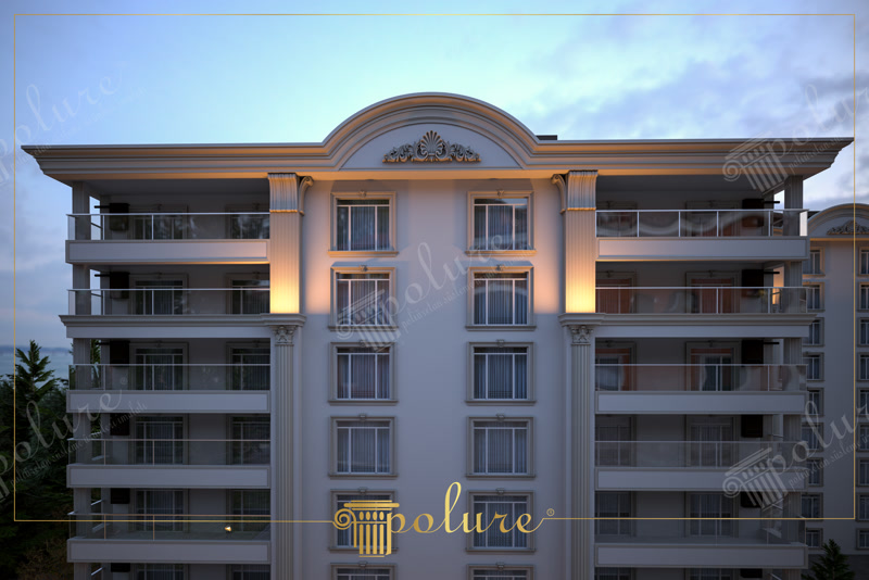 Decoratiuni exterioare din poliuretan pentru fatade multietajate Decorarea fatadelor din poliuretan de inalta densitate reprezinta o solutie tehnica eficienta pentru placarea exterioara a cladirilor rezidentiala multietajate. Materialul avand o densitate medie de 150-220 kg/m³ (țintă ~160 kg/m³) ofera o rezistenta mecanica excelenta la impact si intemperii, fara a suprasolicita structura de rezistenta a cladirii. In aceasta aplicatie pe un edificiu de 6 etaje, profilele verticale de tip pilastru si ancadramentele de ferestre creeaza o geometrie rigida si bine definita, imbinand estetica clasica cu cerintele tehnice moderne de izolatie si durabilitate.

Montajul elementelor arhitecturale din poliuretan pe fatada se realizeaza prin lipire structurala cu adeziv poliuretanic monocomponent si ancorare mecanica suplimentara. Procedeul garanteaza o stabilitate dimensionala optima in intervalul de temperatura de la -100 °C / +80 °C, prevenind aparitia fisurilor la imbinari. Pilatrii canelati instalati intre ferestre asigura continuitate vizuala, iar capitalurile decorative sunt debitate si ajustate precis pe santier folosind scule standard pentru prelucrarea lemnului.

Comportamentul poliuretanului la exterior este net superior elementelor traditionale din beton sau polistiren expansat (EPS), avand o rata de absorbtie a apei de sub 0.1%. Suprafata profilata este pre-amorsata din fabrica, permitand aplicarea directa a vopselelor lavabile de exterior pe baza de rasini acrilice sau siliconice. Frontalul cladirii beneficiaza de un fronton semicircular cu decor reliefat la ultimul nivel, rezistent la razele UV si la ciclurile repetate de inghet-dezghet.

Sistemul de profile decorative din poliuretan permite o instalare rapida, reducand timpul de executie pe fatada cu pana la 50% comparativ cu stucaturile clasice din ipsos sau piatra sintetica. Intretinerea ulterioara necesita doar spalare periodica cu apa sub presiune mica, mentinand aspectul curat pe o durata lunga de exploatare.