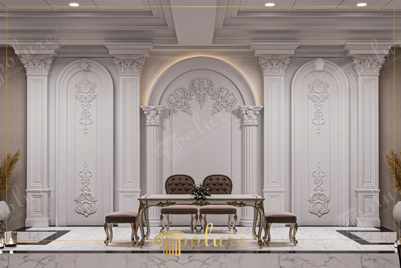 Decoratiuni din Poliuretan Pentru Saloane si Scene Elementele decorative din poliuretan pentru fundaluri de scenă și săli de evenimente reprezintă soluția tehnică ideală pentru crearea structurilor arhitecturale clasice cu greutate redusă și durabilitate ridicată. În această aplicație, ansamblul format din pilastri capitelați, arcada centrală și panourile cu reliefuri florale oferă o rigiditate structurală excelentă datorită densității ridicate a materialului de 150-220 kg/m³ (țintă ~160 kg/m³). Spre deosebire de ipsosul tradițional, spuma poliuretanică cu densitate mare nu se fisurează la vibrații sau variații sezoniere de temperatură, având o toleranță termică cuprinsă între -100 °C / +80 °C.

Procesul de montaj al sistemului decorativ din poliuretan necesită o pregătire riguroasă a suprafeței suport și utilizarea adezivilor structurali specifici. Profilele de încadrare și pilastrii sunt fixați mecanice și prin lipire cu adeziv poliuretanic mono-component, care asigură o legătură chimică extrem de puternică pe zidărie sau gips-carton. Îmbinările dintre elementele individuale sunt tratate cu adeziv special pentru rosturi, urmate de o șlefuire fină cu hârtie abrazivă de granulație 180-240. Această tehnică garantează o suprafață perfect continuă, fără linii vizibile de îmbinare, pregătită complet pentru aplicarea vopselelor lavabile pe bază de apă.

Comportamentul poliuretanului în spații comerciale cu trafic intens este net superior altor materiale decorative, având o rată de absorbție a apei sub 0.5% și o rezistență deosebită la umiditate sau curățare frecventă. În zona arcadei centrale, nișa creată permite integrarea facilă a benzilor LED cu lumină caldă, fără riscul de deformare termică a profilului. Polimerul de înaltă densitate își păstrează stabilitatea dimensională pe termen lung, prevenind apariția spațiilor libere la joncțiunea dintre perete și plintă sau între capiteliu și plafonul casetat.

Detaliile sculpturale complexe, precum ornamentul de coronament al arcadei și ornamentele aplicate pe panourile laterale, sunt obținute prin matrițare de înaltă precizie în tipare metalice. Această tehnologie permite reproducerea fidelă a modelelor neoclasice cu muchii ascuțite și detalii volumetrice profunde, imposibil de realizat economic prin metode tradiționale de tencuire. Suprafața finisată din fabrică cu amorsă albă facilitează aderența optimă a straturilor ulterioare de vopsea satinată sau mată, asigurând o întreținere facilă și un aspect impecabil în exploatarea zilnică.