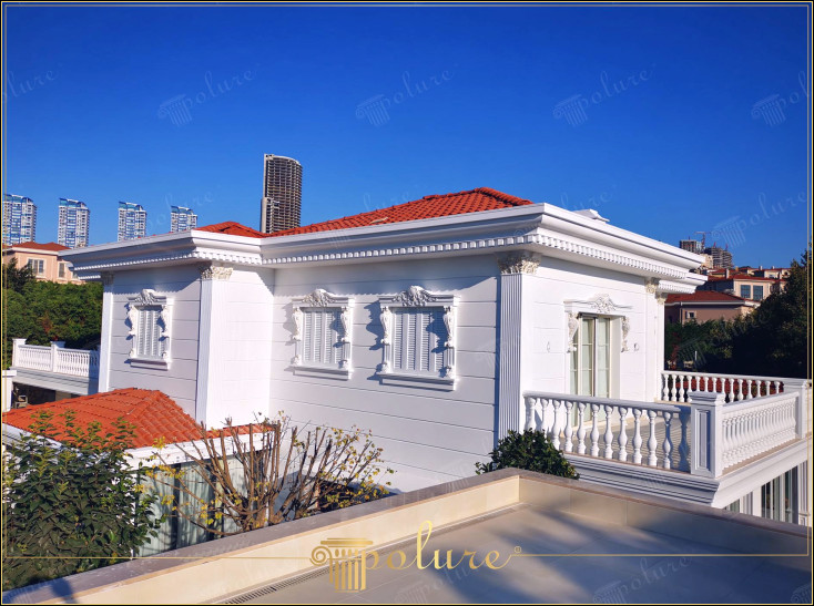 Fațade exterioare cu măreție arhitecturală clasică, îmbogățite cu coloane și detalii din poliuretan Eleganța arhitecturii clasice este evidentă și în clădirile moderne. Vila din această imagine prezintă unul dintre cele mai frumoase exemple de decorare exterioară clasică. Nobilimea albului intalneste coloanele din poliuretan si capitelurile de coloana in stil corintic. În timp ce stâlpii ferestrelor adaugă profunzime detaliilor elegante de pe fațadele exterioare, badastrolul și mulurile de streașină fac silueta caracteristică a clădirii clară. Acoperiri cu panouri din poliuretan Aduce frumusețe de lungă durată fațadelor exterioare, îmbinând estetica tradițională cu avantajele materialelor moderne. Fie că proiectați o clădire nouă sau vă gândiți să adăugați o notă clasică unei case existente, aceste elemente adaugă originalitate și valoare estetică fiecărui proiect.