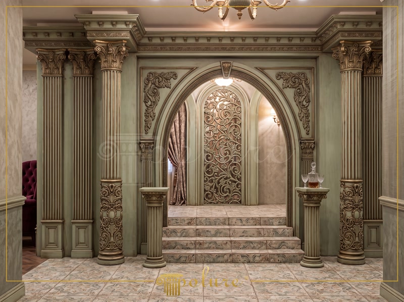 Elemente din Poliuretan pentru Arcade și Coloane Decorative Ansamblurile decorative din poliuretan de înaltă densitate, având o masă volumică cuprinsă între 180 și 150-220 kg/m³ (țintă ~160 kg/m³), oferă o soluție tehnică durabilă și precisă pentru realizarea arcadelor monumentale și a structurilor clasice de interior. Materialul polimeric prezintă o rezistență termică excelentă în intervalul de temperatură -100 °C / +80 °C, având un coeficient de absorbție a apei de sub 1%, ceea ce previne apariția fisurilor sau deformărilor în timp. În această configurație arhitecturală, cadrul include coloane canelate complet echipate cu capiteluri ornamentale, ancadramente arcuite și panouri decorative filigranate. Flexibilitatea profilelor sintetice permite executarea razelor complexe de curbură fără a compromite integritatea detaliilor sculpturale ale materialului.

Montajul arcadelor formate din profile flexibile p85002-flex și p82083-flex necesită o pregătire riguroasă a suprafeței suport și utilizarea unui adeziv structural poliuretanic special pentru îmbinări. Pentru garantarea unei fixări mecanice optime pe durata procesului de polimerizare a adezivului, se recomandă utilizarea șuruburilor de ancorare temporară, amplasate la un pas tehnic de 150-200 mm de-a lungul razei de curbură. Profilele flexibile p85409-flex sunt folosite pentru conturarea ramelor pe perete, preluând cu precizie neregularitățile suprafeței și asigurând o aliniere geometrică perfectă pe toate axele de montaj.

Tratamentul de finisare al profilelor din poliuretan începe după maturarea completă a adezivului de îmbinare, proces ce durează aproximativ 24 de ore la o temperatură ambientală de 20°C. Rosturile și punctele de îmbinare se șlefuiesc mecanic sau manual utilizând hârtie abrazivă cu granulație fină de 240-320 pentru obținerea unei suprafețe perfect uniforme. Panoul ornamental p82022-flex integrat în fundal este fixat pe structura din zidărie sau gips-carton, fiind pregătit pentru aplicarea straturilor de grund acrilic și a vopselelor lavabile. Tehnica de patinare cu pigmenți în nuanțe de verde antic și accente aurii scoate în relief adâncimea detaliilor decorative.

Spre deosebire de ipsosul tradițional sau elementele din lemn masiv, componentele din poliuretan au o greutate redusă și nu își modifică volumul în condiții de umiditate variabilă. Această stabilitate dimensională facilitează un proces de instalare rapid și curat pe șantier, reducând semnificativ timpul de execuție al proiectelor de amenajare. Rezistența mecanică la impact moderat și compatibilitatea cu o gamă largă de finisaje fac din poliuretan alegerea tehnică optimă pentru echipele de montaj și contractorii din domeniul amenajărilor interioare.