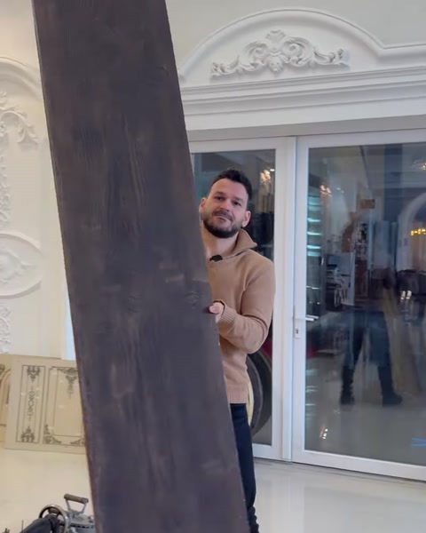 Bărbat sprijină o grindă lungă închisă la culoare lângă vitrină