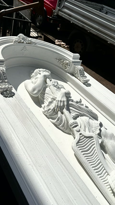 Sculptură înaripată sub arcadă decorată cu motive florale