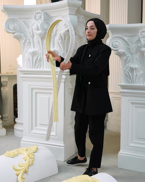 Femeie prezintă profilul flexibil curbat lângă coloanele decorative din fundal.