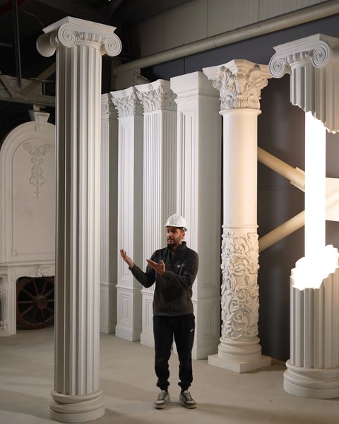 Bărbat gesticulează lângă mai multe coloane finisate în atelier