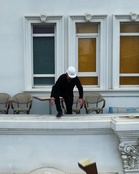 Muncitor cu cască inspectează balconul clădirii unde stau scaune
